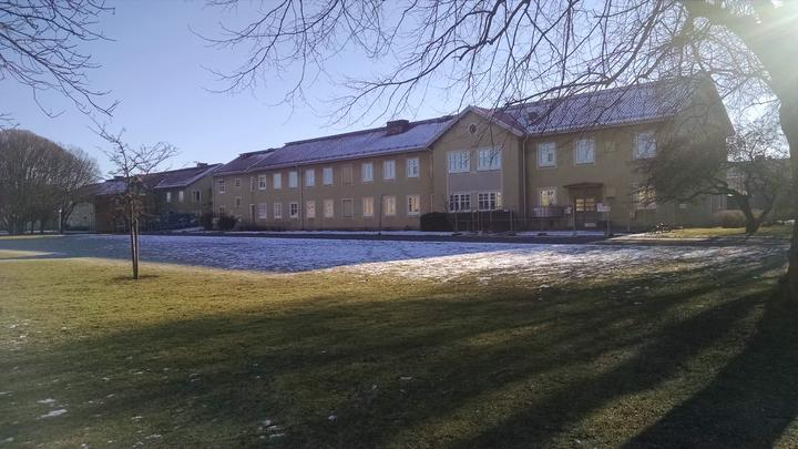 a long, flat building with living quarters on a clear day with a light snow on the grassy front yard